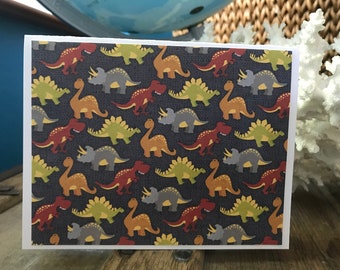 May include: A card with a repeating pattern of colorful dinosaurs on a dark gray background. The dinosaurs are in various poses, including standing, walking, and running.