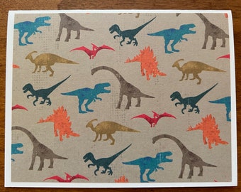May include: A beige card with a repeating pattern of brown, blue, green, and orange dinosaurs. The dinosaurs are in various poses, including walking, running, and standing. The card has a subtle speckled texture.