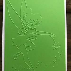 May include: A green card with a white outline of Tinkerbell, a fairy with wings, holding a wand with sparkles. The background is green with white sparkles.