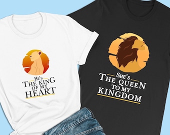Może przedstawiać: Dwie koszulki z grafiką lwa i tekstem. Biała koszulka z napisem "He's The King Of My Heart". Czarna koszulka z napisem "She's The Queen To My Kingdom".