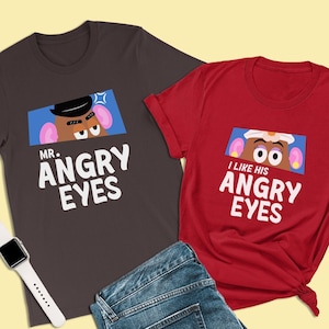 Può includere: Due t-shirt con un tema di Mr. Potato Head. La t-shirt grigio scuro dice "Mr. Angry Eyes" e presenta un'immagine di cartone animato di Mr. Potato Head con un'espressione arrabbiata. La t-shirt rossa dice "I Like His Angry Eyes" e presenta un'immagine di cartone animato di Mrs. Potato Head con un'espressione sorpresa.
