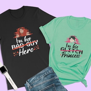 May include: Two t-shirts with a pixelated design. The black t-shirt has a red character with the text "I'm her Bad Guy Hero" and the green t-shirt has a blue character with the text "I'm his Glitch Princess".
