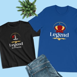 May include: Two t-shirts with different designs. The black t-shirt has a sword and the text "Legend in Process". The blue t-shirt has a crown and the text "Legend".