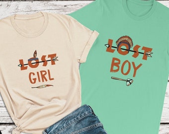 May include: Two t-shirts, one beige and one teal green, with the text "Lost Girl" and "Lost Boy" printed on them. Both shirts feature an arrow and a Native American headdress graphic.