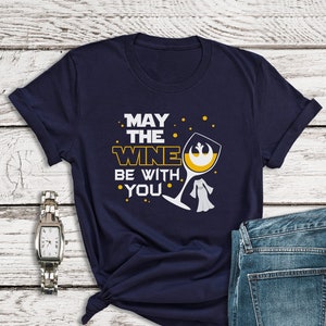 Op de afbeelding: Een marineblauw T-shirt met een witte afbeelding van een wijnglas met een Star Wars Rebel Alliance-symbool. De tekst op het shirt luidt "Moge de wijn met je zijn."