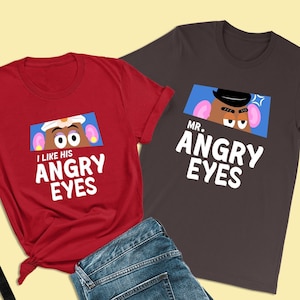 Può includere: Due magliette, una rossa e una grigio scuro, con un'immagine di cartone animato di Mr. e Mrs. Potato Head. La maglietta rossa dice "Mi piacciono i suoi occhi arrabbiati" e la maglietta grigia dice "Mr. Occhi arrabbiati".