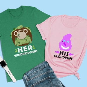 以下が含まれることがあります： 緑とピンクの色の組み合わせのTシャツ2枚。緑のTシャツには、緑と茶色のウィンドブレーカーを着た漫画の猿と「HER WINDBREAKERS」の文字が書かれている。ピンクのTシャツには、顔のある漫画の紫色の雲と「HIS CLOUDPUFF」の文字が書かれている。