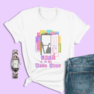 May include: White t-shirt with a colorful graphic of a couple dancing in front of an open door. The text "LOVE is an OPEN DOOR" is printed below the graphic.