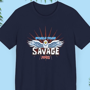 May include: A navy blue t-shirt with a graphic of a white eagle with blue wings, a red and white starburst, and the text "WORLD TOUR SAVAGE 1992".
