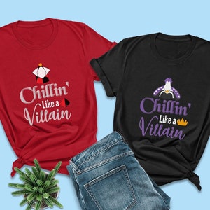 Puede incluir: Dos camisetas con un dise&ntilde;o en negro y rojo. La camiseta roja tiene una silueta blanca de la Reina de Corazones con una corona y una carta de juego. La camiseta negra tiene una silueta morada de &Uacute;rsula con una corona. Ambas camisetas tienen el texto "Chillin' Like a Villain" en letras blancas y moradas.
