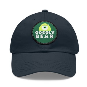 May include: A navy blue baseball cap with a green and yellow embroidered patch that says "GOOGLY BEAR".