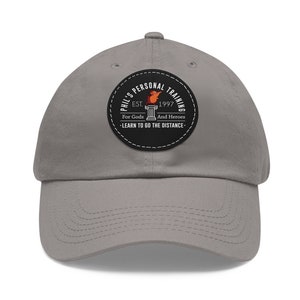 May include: Gray baseball cap with a black and white patch that says "Phil's Personal Training Est. 1997 For Gods And Heroes -Learn To Go The Distance-"