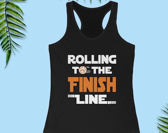 Puede incluir: Camiseta de tirantes negra con un gráfico blanco que dice "Rolling to the Finish Line" con un pequeño balón de fútbol naranja.