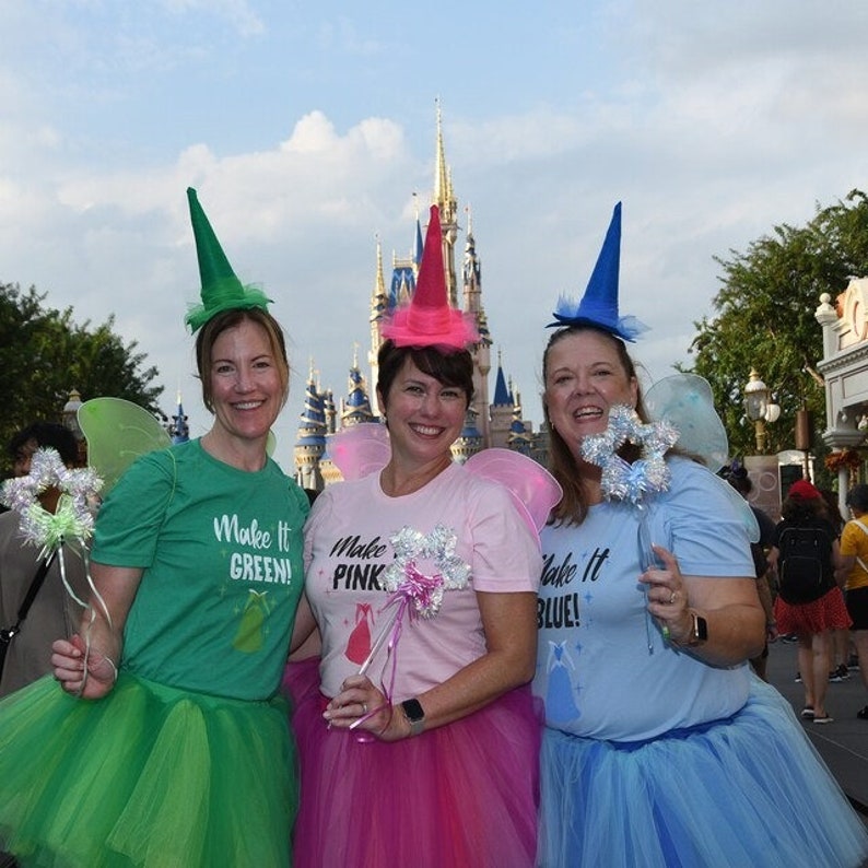 Puede incluir: Tres mujeres vestidas de hadas frente al Castillo de Cenicienta en Walt Disney World. Llevan tut&uacute;s verdes, rosas y azules y camisas a juego que dicen "Make it Green!", "Make it Pink!" y "Make it Blue!"