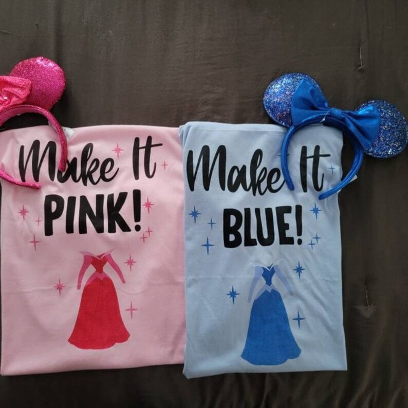 Puede incluir: Dos camisetas con el texto "Make it Pink!" y "Make it Blue!" impreso en ellas. Cada camiseta presenta una princesa de dibujos animados con un vestido, uno rosa y otro azul. Las camisetas est&aacute;n acompa&ntilde;adas por un par de orejas de rat&oacute;n rosas y un par de orejas de rat&oacute;n azules.