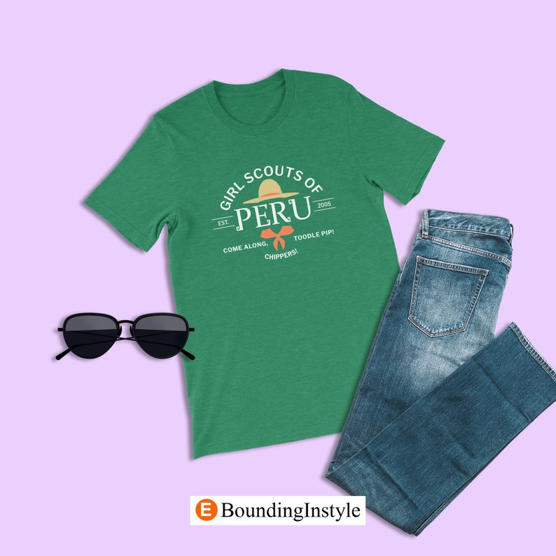 May include: Green t-shirt with a white graphic of a Girl Scouts of Peru logo. The logo features a straw hat and the text "Girl Scouts of Peru" with the text "Est. 2005" and "Come Along, Toodle Pip! Chippers!" underneath.