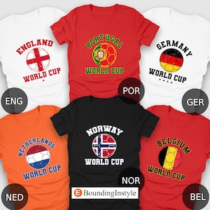 May include: A collection of short-sleeved t-shirts in various colors, each featuring a soccer ball design and the name of a country. The shirts include England, Portugal, Germany, Netherlands, Norway, and Belgium, with "World Cup" text.