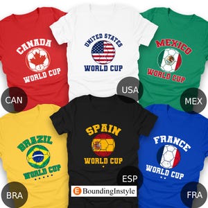 May include: A collection of t-shirts in various colors, each featuring a soccer ball design with the text "WORLD CUP" and the names of different countries: Canada, United States, Mexico, Brazil, Spain, and France.