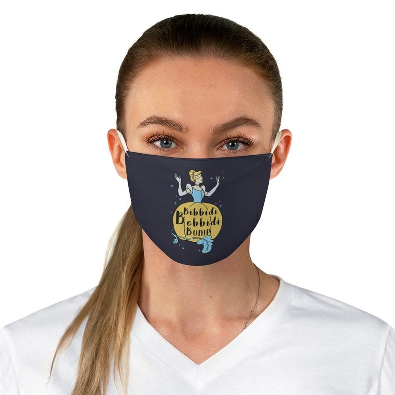 May include: A blue face mask with a yellow pumpkin and a cartoon image of Cinderella. The text on the mask reads "Bibbidi Bobbidi Boo"