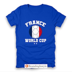 May include: Royal blue t-shirt featuring a soccer ball design in the colors of the French flag. The text "FRANCE" is arched above the ball, with "WORLD CUP" below. Two small stars are beneath the text.