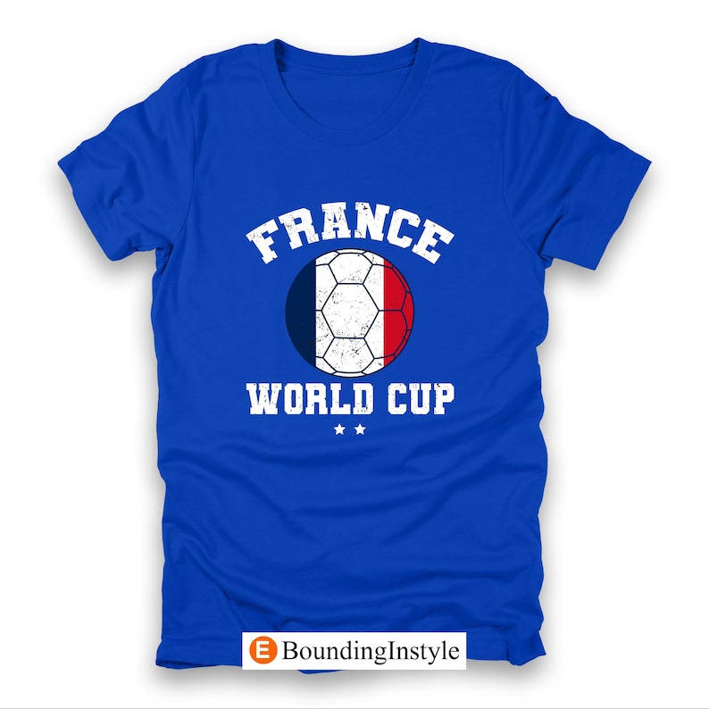 May include: Royal blue t-shirt featuring a soccer ball design in the colors of the French flag. The text "FRANCE" is arched above the ball, with "WORLD CUP" below. Two small stars are beneath the text.