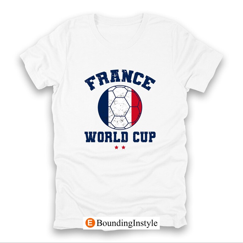 May include: White t-shirt featuring a soccer ball design in the colors of the French flag. The text "FRANCE WORLD CUP" is printed above and below the ball in a distressed navy blue font. Two small red stars are below the text.