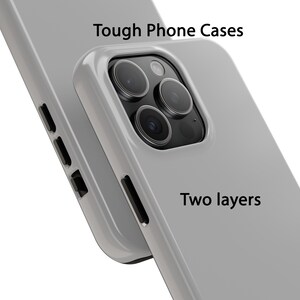 K&ouml;nnte beinhalten: Zwei graue Handyh&uuml;llen mit einem Ausschnitt f&uuml;r das Kameraobjektiv. Der Text "Tough Phone Cases" und "Two layers" ist auf den H&uuml;llen aufgedruckt.