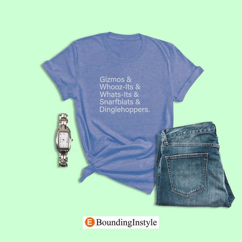 May include: A blue t-shirt with the text "Gizmos & Whooz-Its & Whats-Its & Snarfblats & Dinglehoppers." The shirt is folded and laid on a green surface with a silver watch and blue jeans.