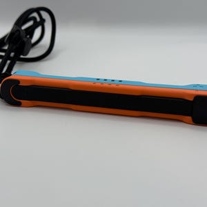 May include: A blue and orange electronic device with a black center section and a black cord. The device has a rectangular shape with rounded ends. The cord is looped and attached to the device.