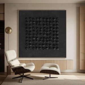 May include: A black and white abstract art print featuring a grid of circles. The print is displayed on a wall in a contemporary living room with a white armchair and footstool.