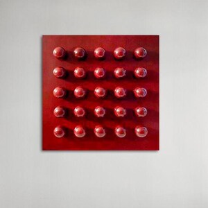 May include: A square, red abstract artwork with a grid of thirty-two raised, spherical shapes. The spheres are a darker shade of red than the background, creating a textured, dimensional effect. The artwork is mounted on a white wall.