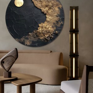May include: A round, black and gold abstract painting with a textured surface. The painting is hanging on a wall in a living room setting.