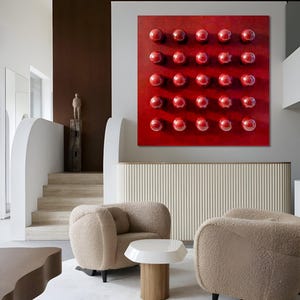 May include: A contemporary living room with a striking red artwork adorned with a grid of glossy spheres. Two beige, curved armchairs rest on a white rug, with a small white and wood side table. The room's design features a neutral colour scheme.