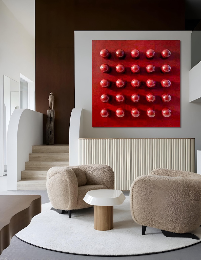 May include: A contemporary living room with a striking red artwork adorned with a grid of glossy spheres. Two beige, curved armchairs rest on a white rug, with a small white and wood side table. The room's design features a neutral colour scheme.
