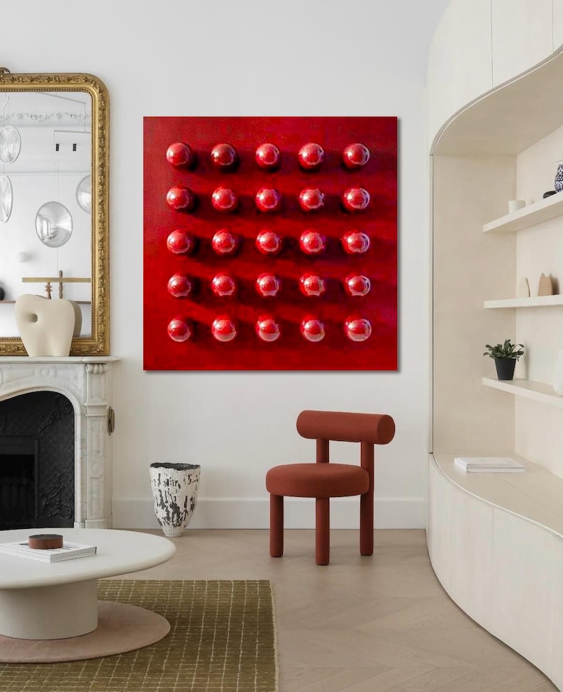 May include: A contemporary interior with a striking red artwork adorned with numerous raised spheres. A small, terracotta-hued chair is positioned in front of the artwork. The room also features a white coffee table, a gold-framed mirror, and a decorative vase.