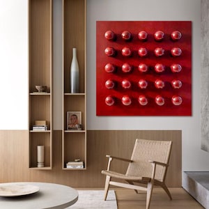 May include: A contemporary living room with a striking red artwork displaying 25 red spheres. The room features a wooden chair with a woven seat, a circular coffee table, and built-in wooden shelves with decorative items.