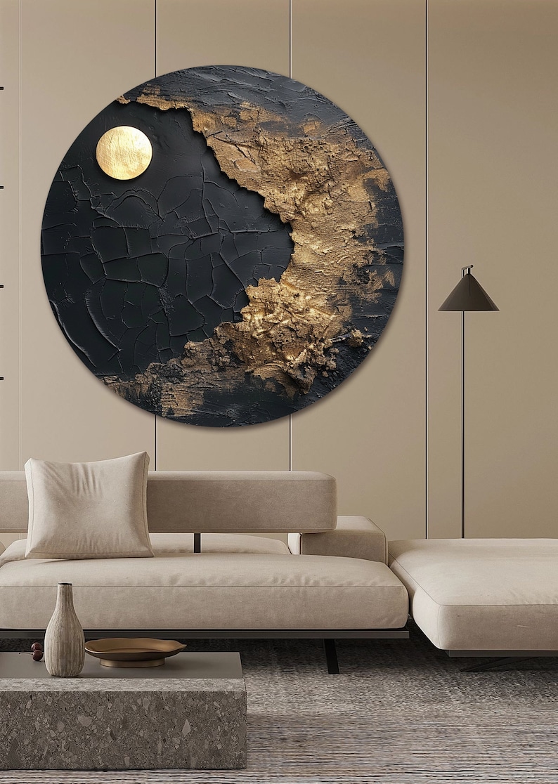 May include: A circular abstract painting with a black and gold color scheme. The painting features a textured surface with a cracked effect. The gold portion of the painting is textured and appears to be raised from the surface. The painting is hanging on a beige wall above a beige couch.