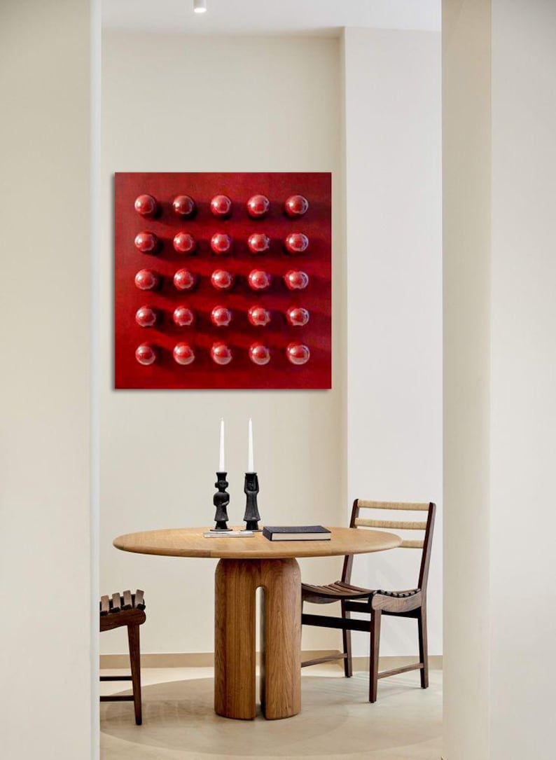 May include: A contemporary dining room with a round wooden table and two chairs. A red square artwork with evenly spaced, raised red spheres hangs on the wall. Two black candle holders with white candles are on the table.