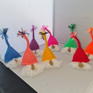 Könnte beinhalten: Eine Sammlung von neun gehäkelten Gnom-Ornamenten in verschiedenen Farben, darunter Blau, Rosa, Lila, Gelb, Grün, Orange und Rot. Jeder Gnom hat einen weißen Bart und eine spitze Mütze.