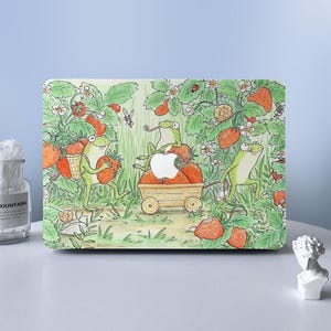 以下が含まれることがあります： イチゴを収穫するカエルの気まぐれなイラストが描かれたラップトップケース。デザインには、バスケットを運ぶカエル、リンゴのカートを引くカエル、イチゴを持って走るカエルが含まれています。背景はイチゴの植物と花でいっぱいです。