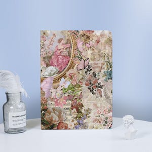 May include: A vintage-inspired notebook cover with a collage of floral patterns, butterflies, and a woman in a dress. The cover features a gold frame and a musical score.