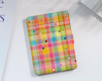 Könnte beinhalten: Eine rechteckige E-Reader-Hülle mit einem lebhaften Karomuster in Gelb-, Rosa-, Blau- und Grüntönen. Die Oberfläche ist mit zahlreichen kleinen, verstreuten sternförmigen Aufklebern in verschiedenen Farben wie Rot, Blau und Silber verziert.
