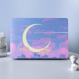 May include: A rectangular laptop skin featuring a vibrant illustration of a large yellow crescent moon set against a sky filled with soft pink, purple, and blue clouds. The design includes a stylized city silhouette at the bottom edge.
