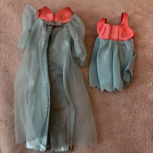 May include: A vintage doll's outfit featuring a light blue robe with sheer sleeves and a matching dress. The robe has a coral-colored bow detail at the neckline. The dress has a coral bodice and a light blue skirt.