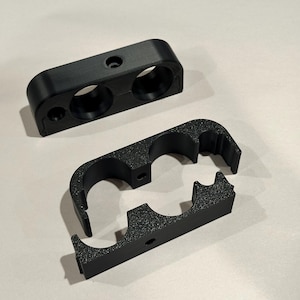 May include: Two black plastic cable clamps, one with two holes and the other with two loops. The clamps are designed to hold cables in place.