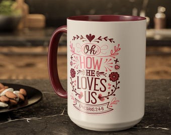 Könnte beinhalten: Weiße Keramiktasse mit einem burgunderfarbenen Rand und Henkel. Die Tasse zeigt ein pinkfarbenes und rotes Design mit dem Text "Oh How He Loves Us" und "Epheser 2:4-8".
