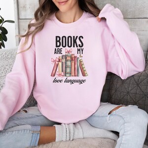 May include: Pink sweatshirt with the text "BOOKS ARE MY LOVE LANGUAGE" and a stack of books with bows and a butterfly.