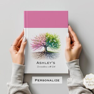 以下が含まれることがあります： ピンクと白のジャーナルで、木のイラストと「Ashley's Conversations with God」というテキストが書かれています。