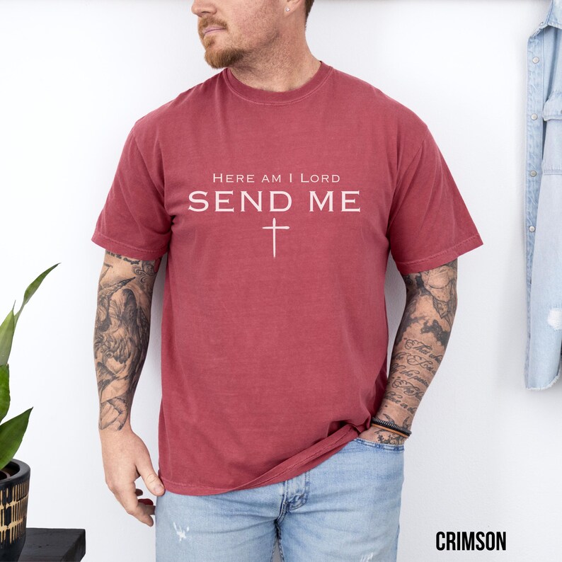 May include: A red t-shirt with the text "Here am I Lord Send Me" and a white cross.