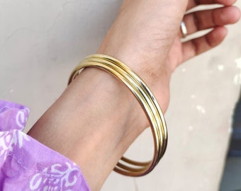 May include: Three gold bangle bracelets stacked on a person's wrist.